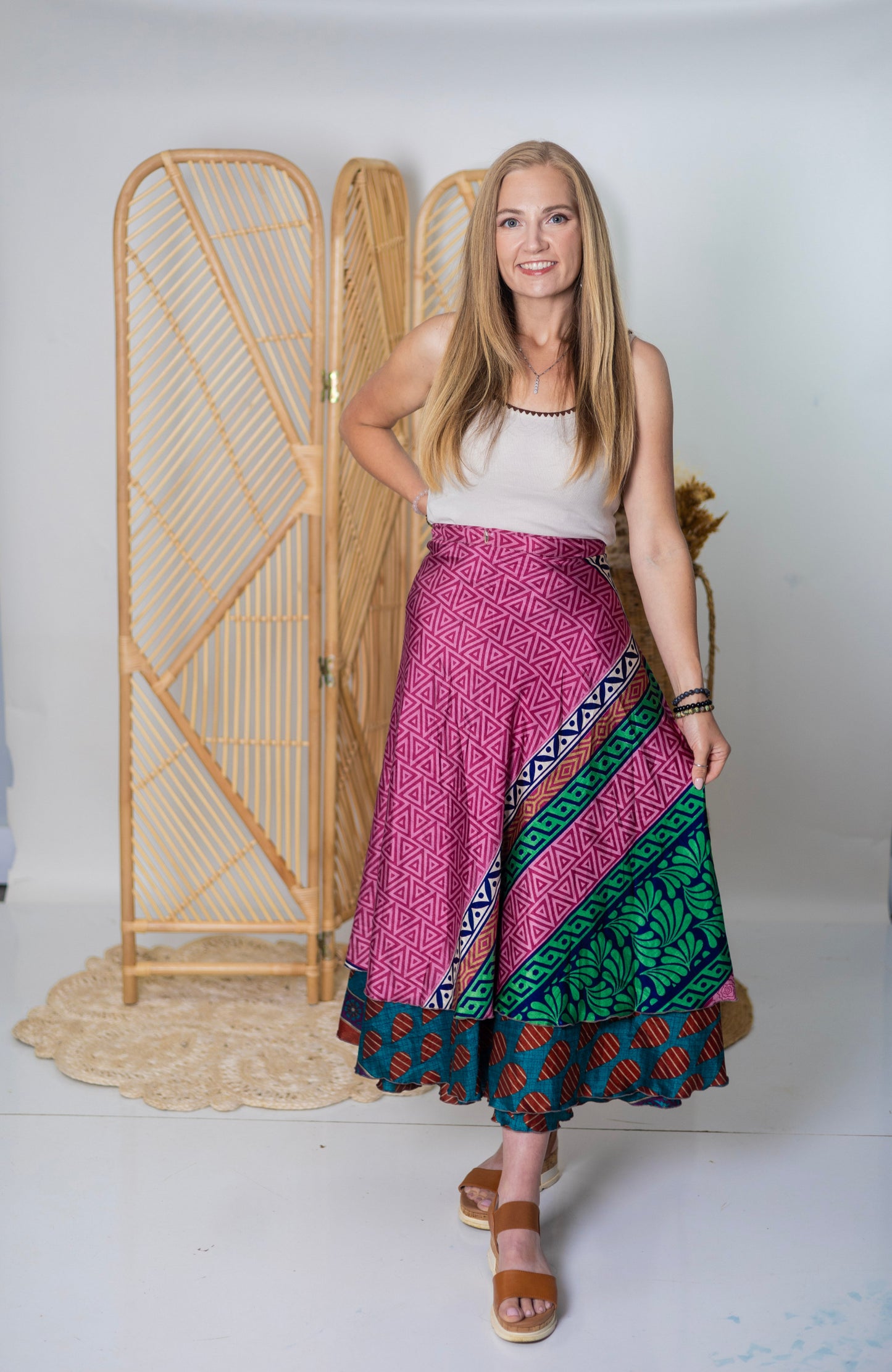 Woman wearing a colorful patterned skirt standing in front of a wooden screen.