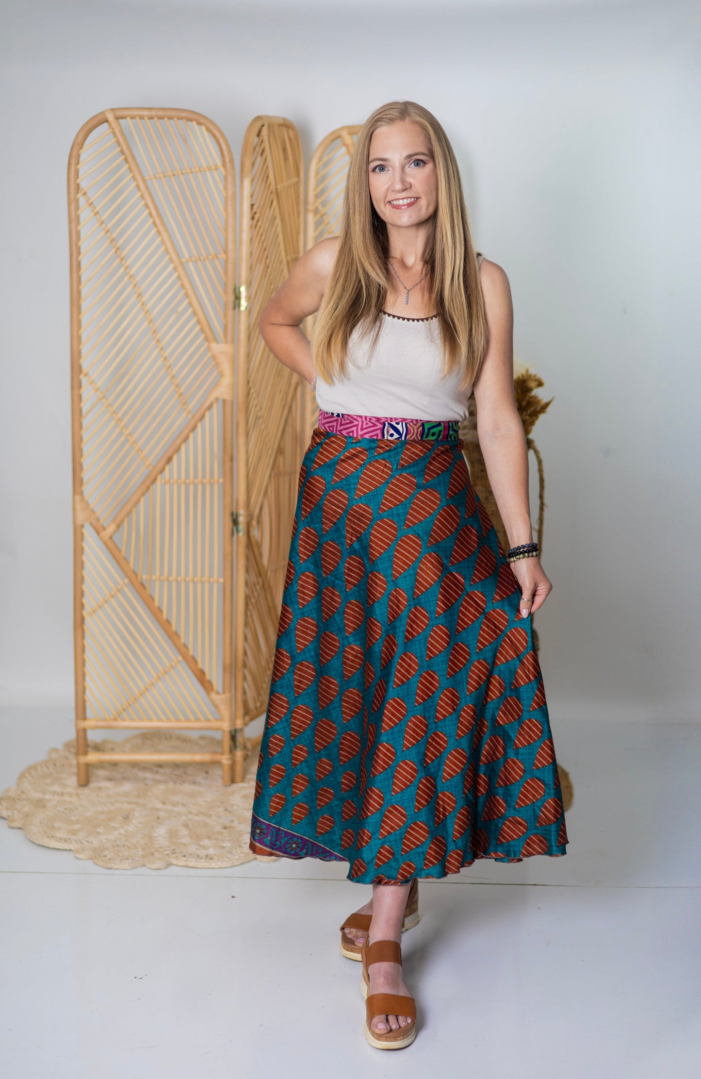 Woman wearing a patterned skirt standing in front of a bamboo screen.