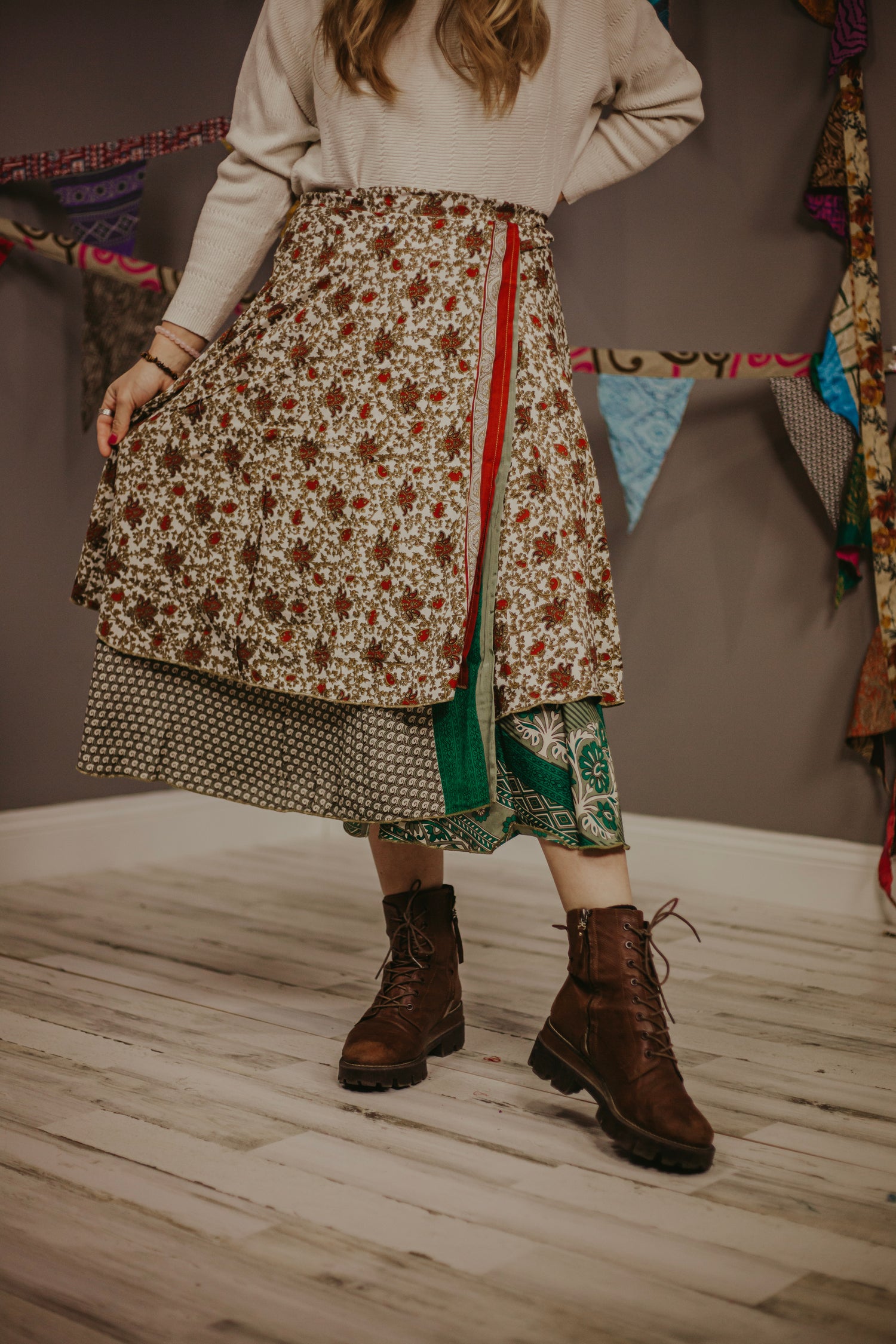 Woman in a cream colored sweater and a tiered wrap skirt with brown combat boots